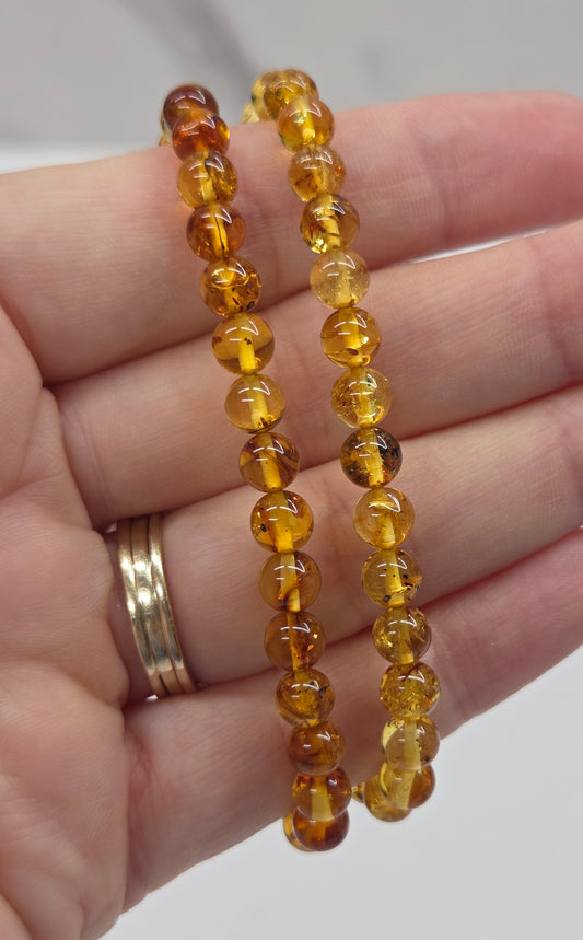 Yellow amber beaded braclet being held in a hand against a white background