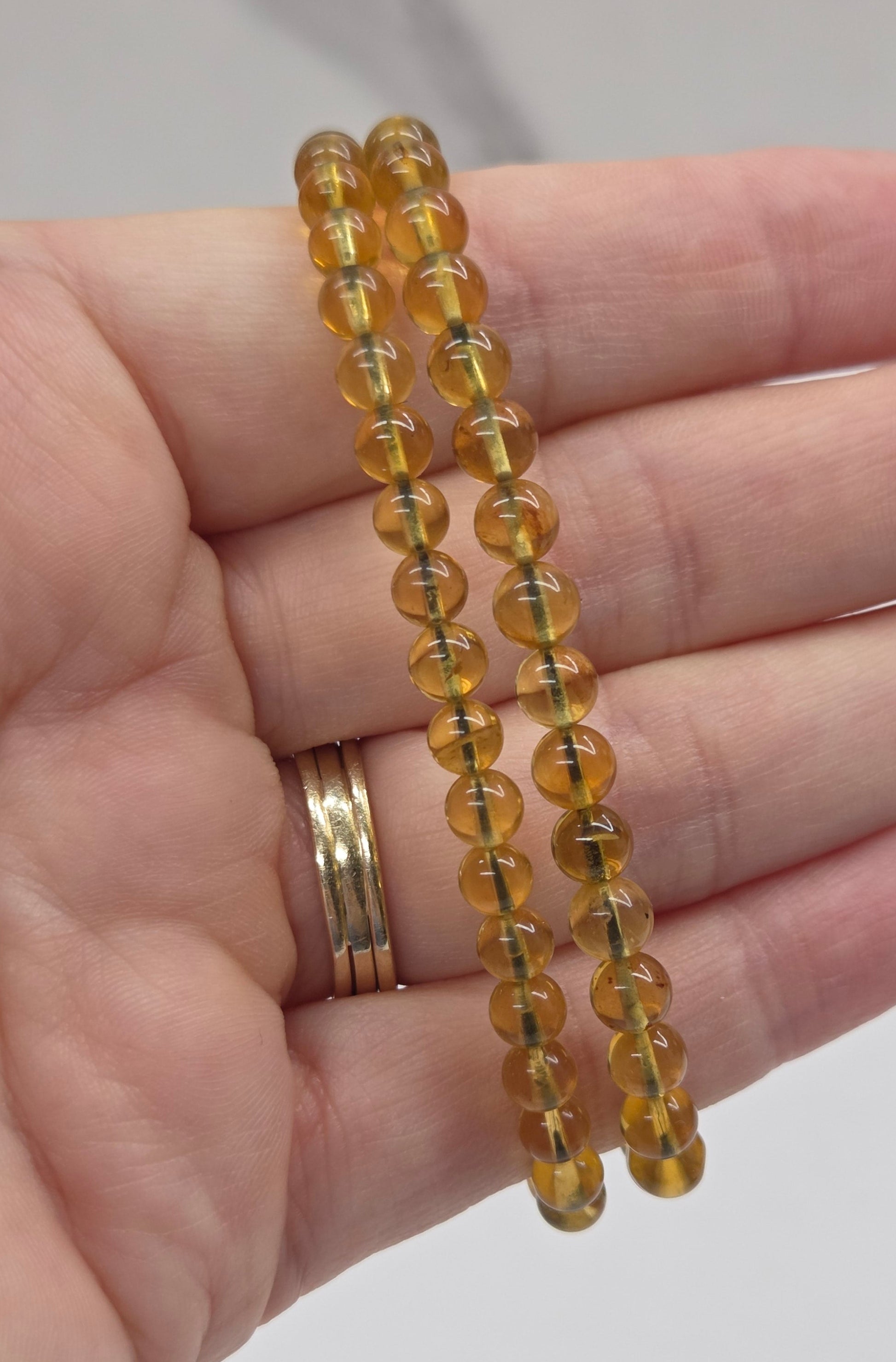 Yellow amber beaded braclet being held in a hand against a white background