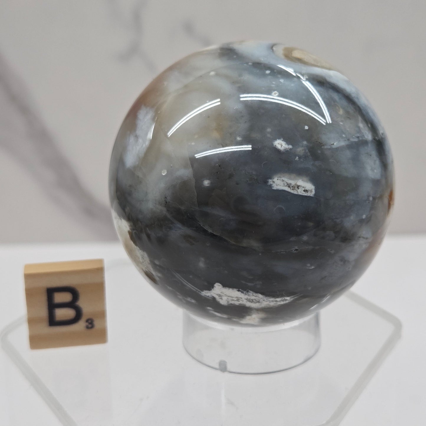 Petrified wood sphere with multiple colors on an acrylic stand against a white background