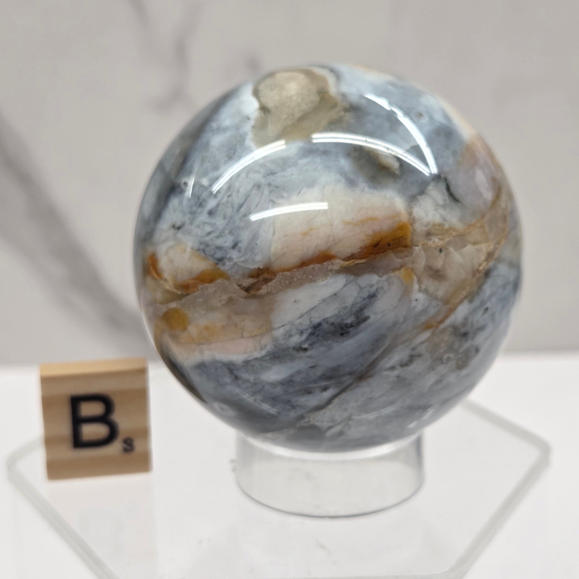 Petrified wood sphere with multiple colors on an acrylic stand against a white background