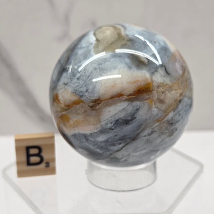 Petrified wood sphere with multiple colors on an acrylic stand against a white background
