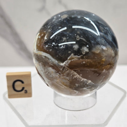 Petrified wood sphere with multiple colors on an acrylic stand against a white background