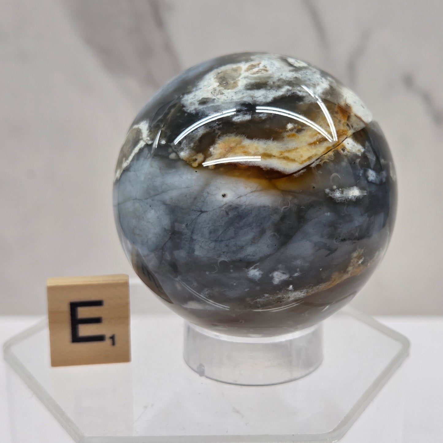 Petrified wood sphere with multiple colors on an acrylic stand against a white background