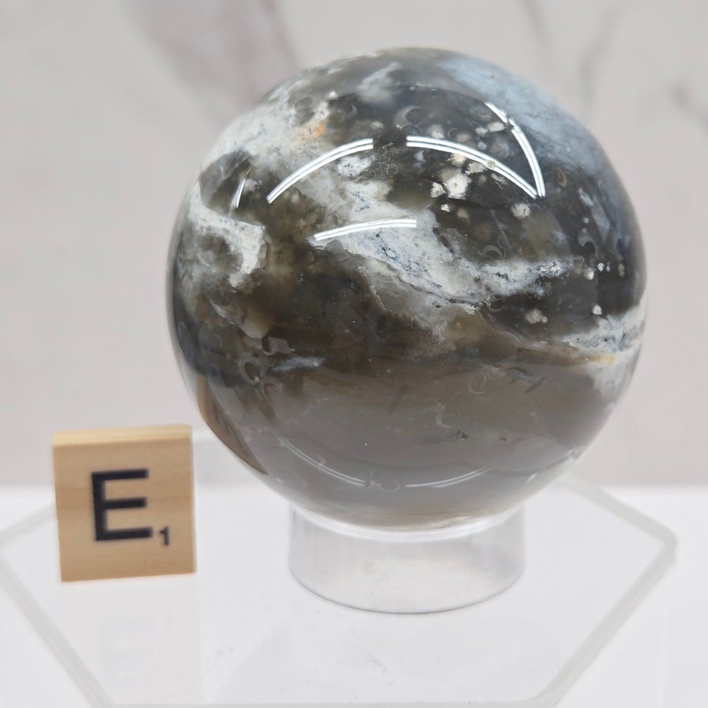Petrified wood sphere with multiple colors on an acrylic stand against a white background
