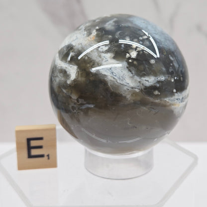 Petrified wood sphere with multiple colors on an acrylic stand against a white background