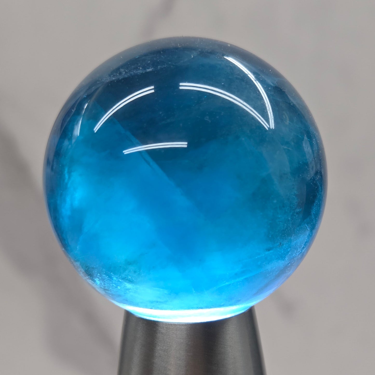 A close-up of a hand holding a metallic silver cylindrical object with a translucent blue spherical end against a light marble background.