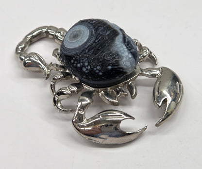 A silver-toned lobster-shaped pendant or charm featuring a dark, marbled black and gray stone cabochon on its back, set against a plain light background.