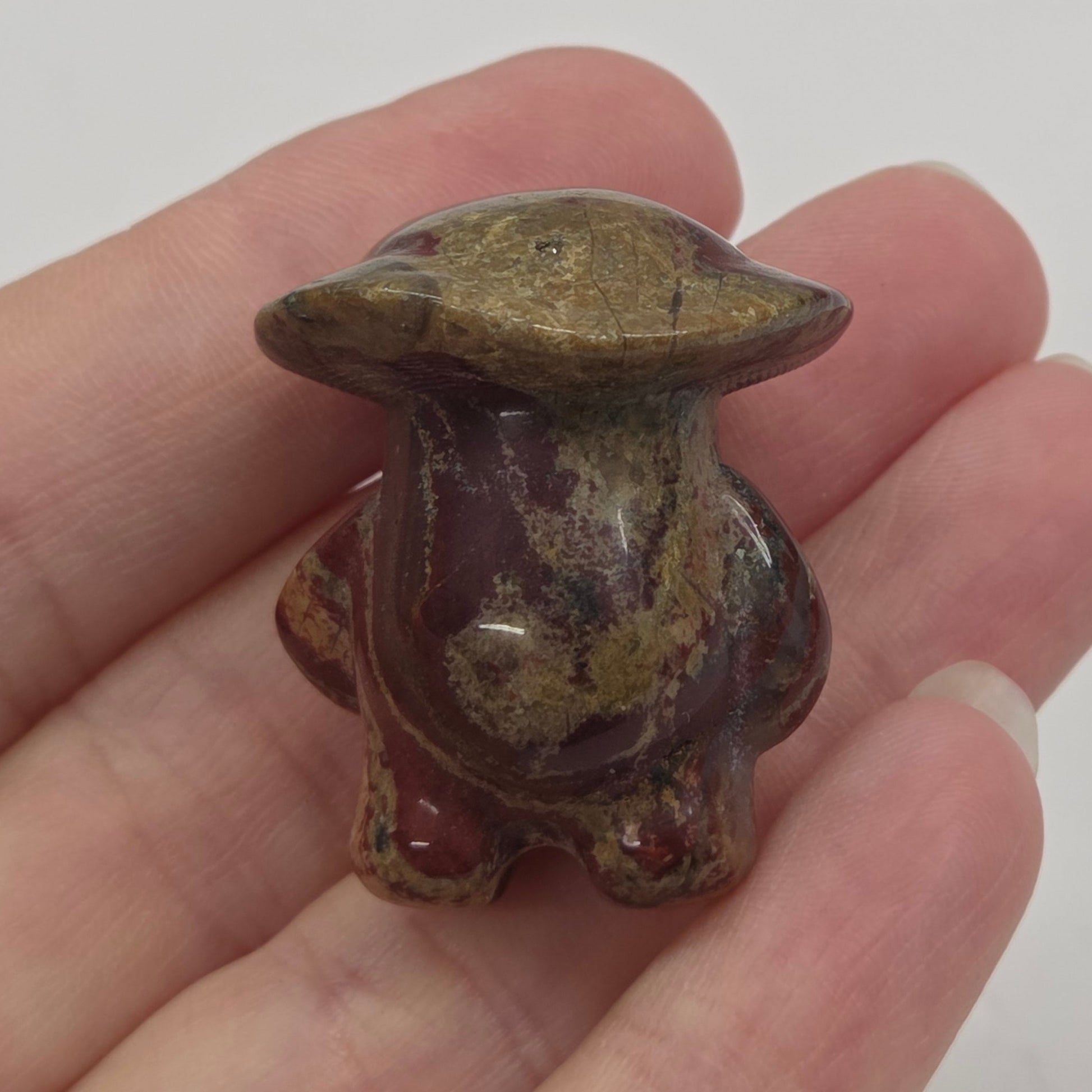 Mushroom man carving with red and brown coloring being held in a hand against a white background