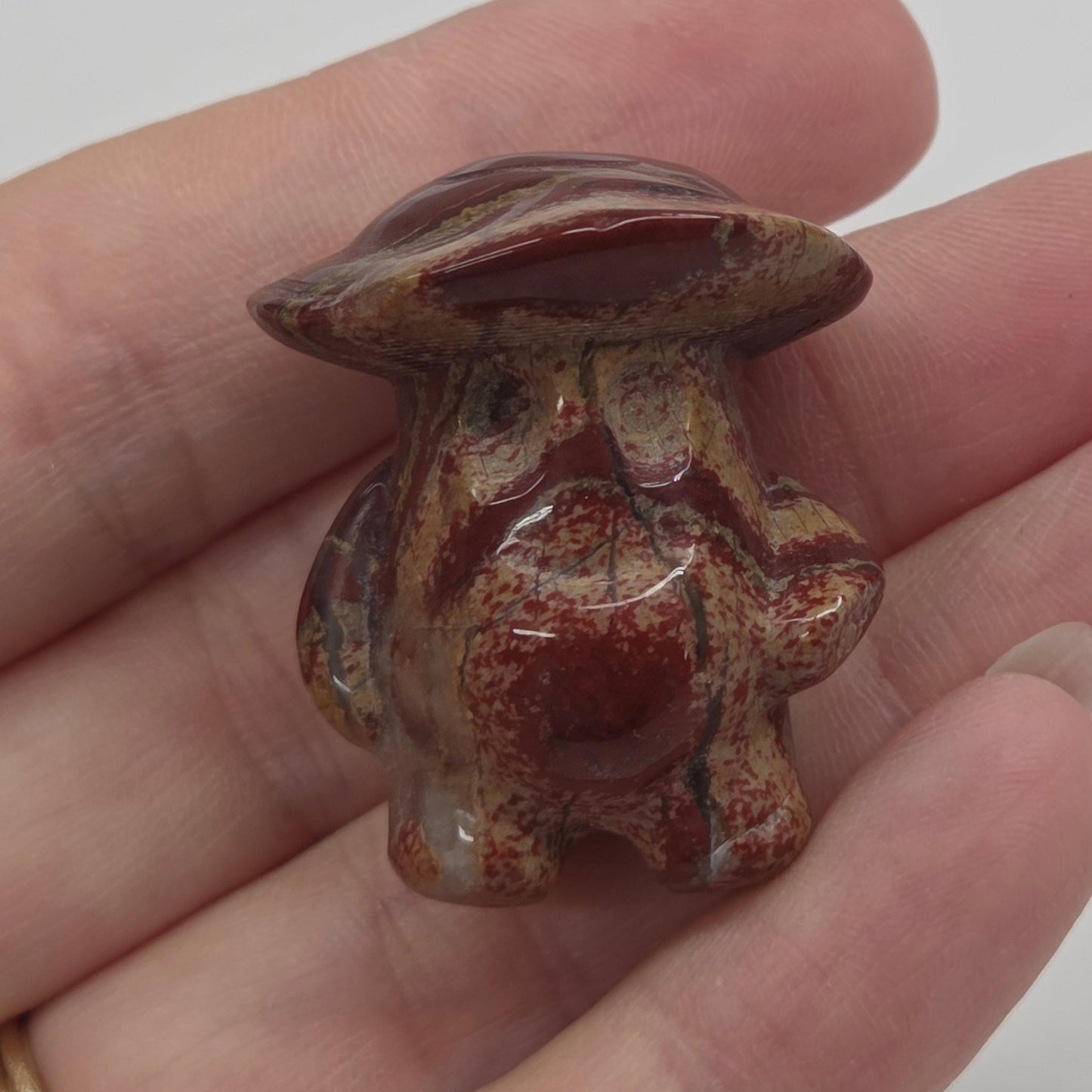 Mushroom man carving with red and brown coloring being held in a hand against a white background