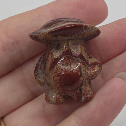 Mushroom man carving with red and brown coloring being held in a hand against a white background