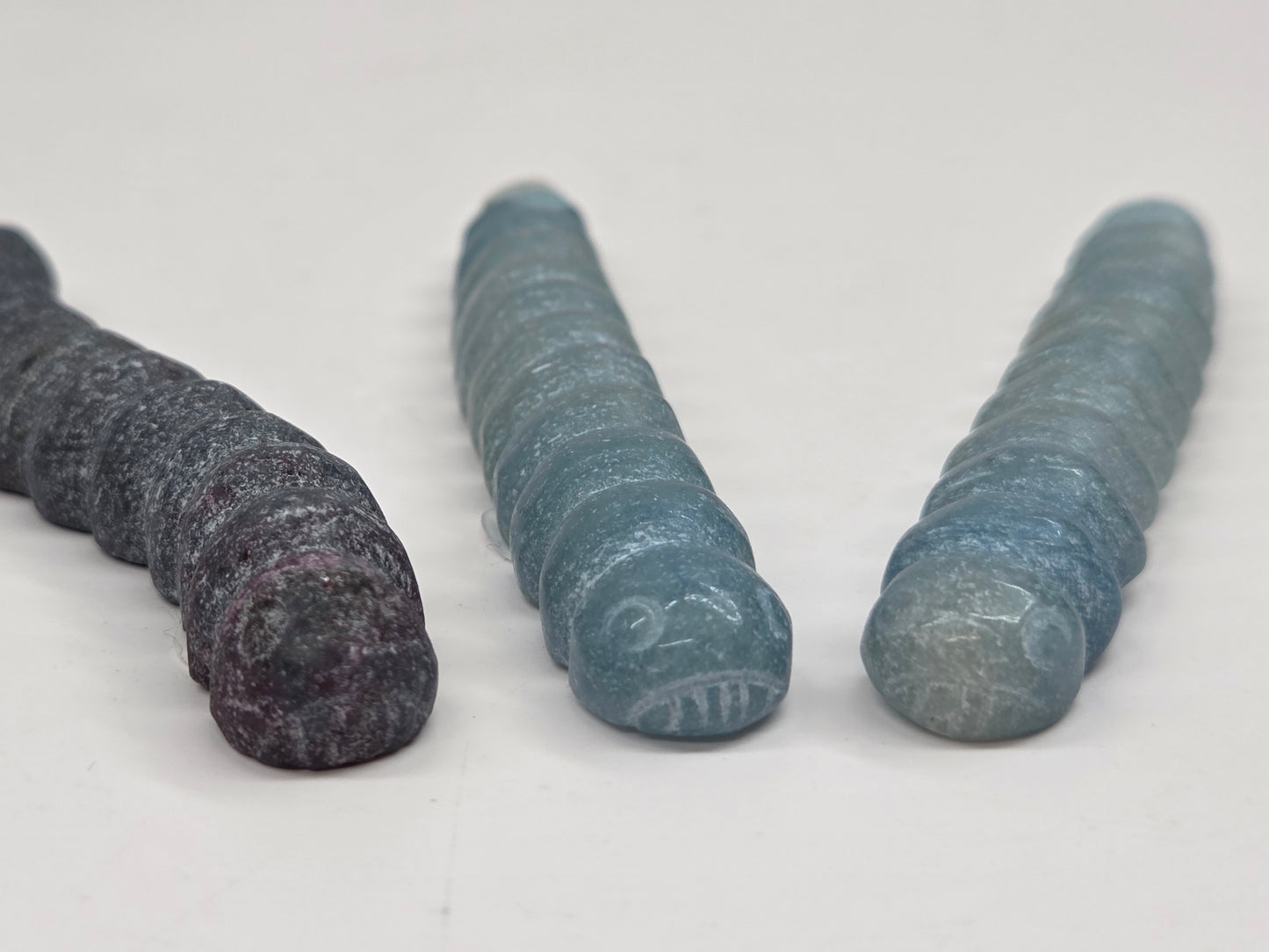 Close-up of crystal worm-like sculptures with face carvings on a white background