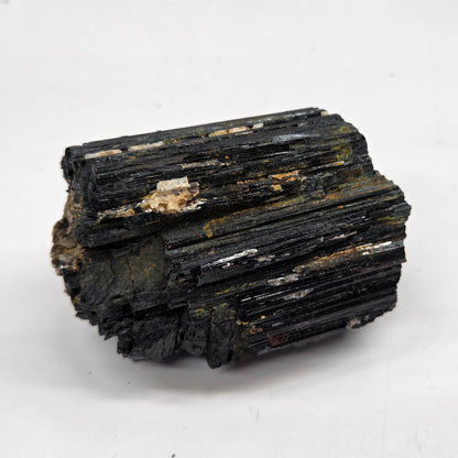 rough black mineral or crystal specimens with some brownish-yellow matrix, arranged on a white surface with a light gray marble-patterned background.