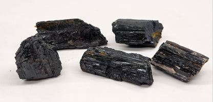 Five rough black mineral or crystal chunks with a glossy, layered texture arranged on a plain white surface.