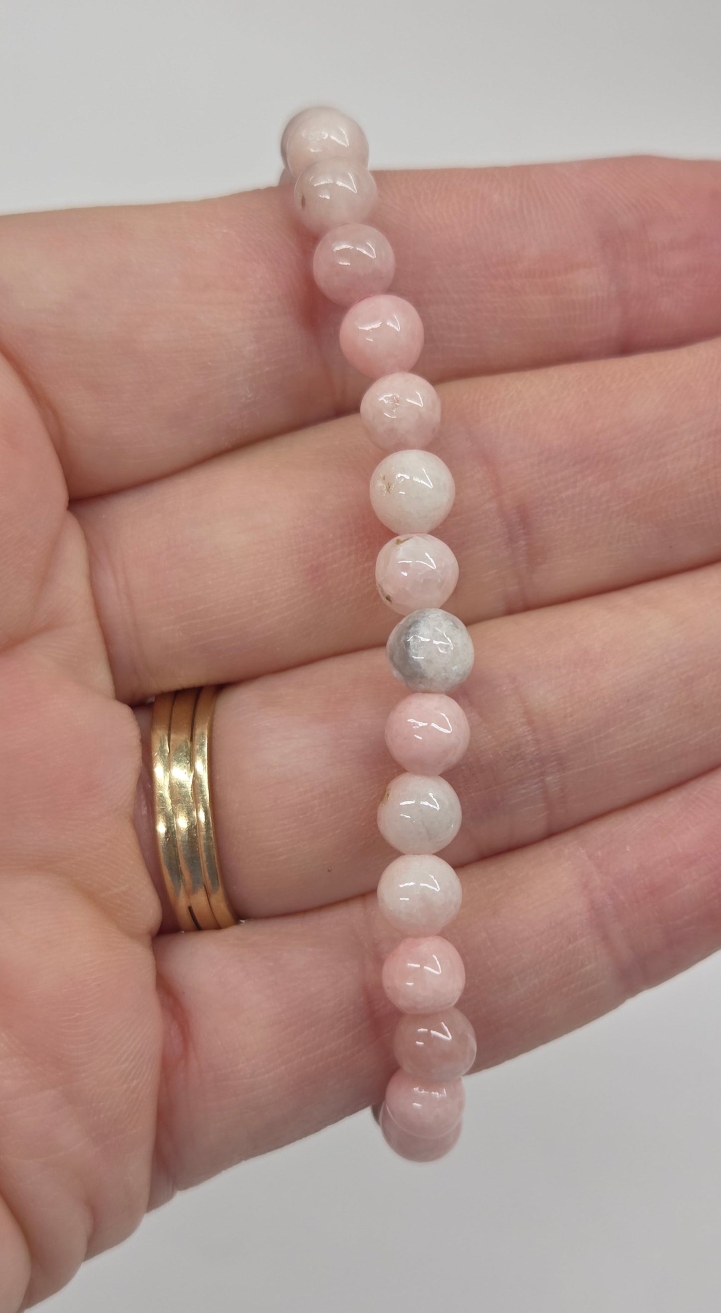 A beaded stretch bracelet made of small round pale pink and white beads, shown resting across an open hand. The hand also wears two gold rings.
