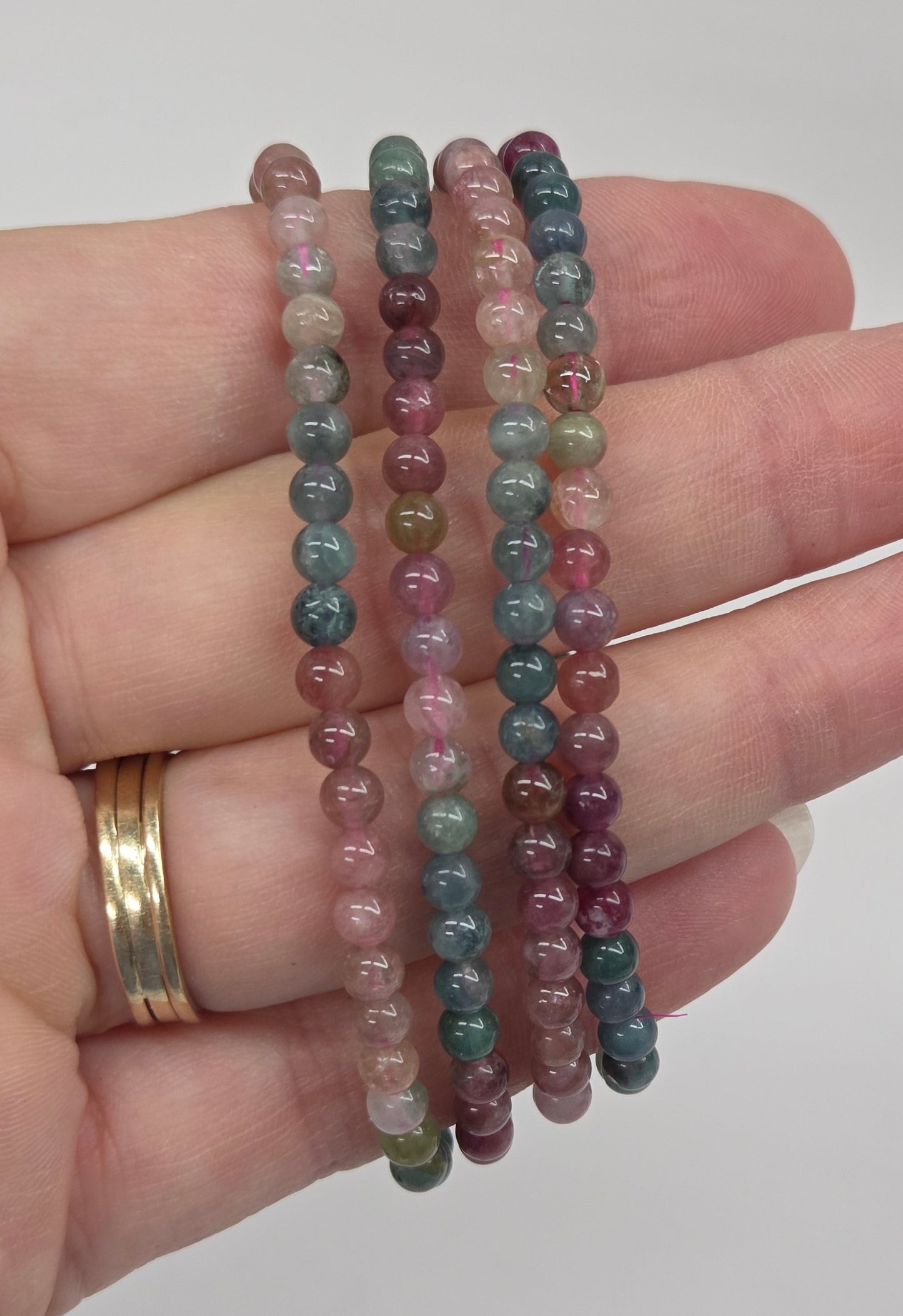 Four beaded stretch bracelets in earthy multicolor shades, held on a person's hand against a plain light gray background.