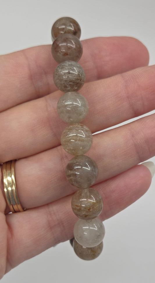 A beaded stretch bracelet made of translucent brown and gray round beads, shown resting on a person's hand.