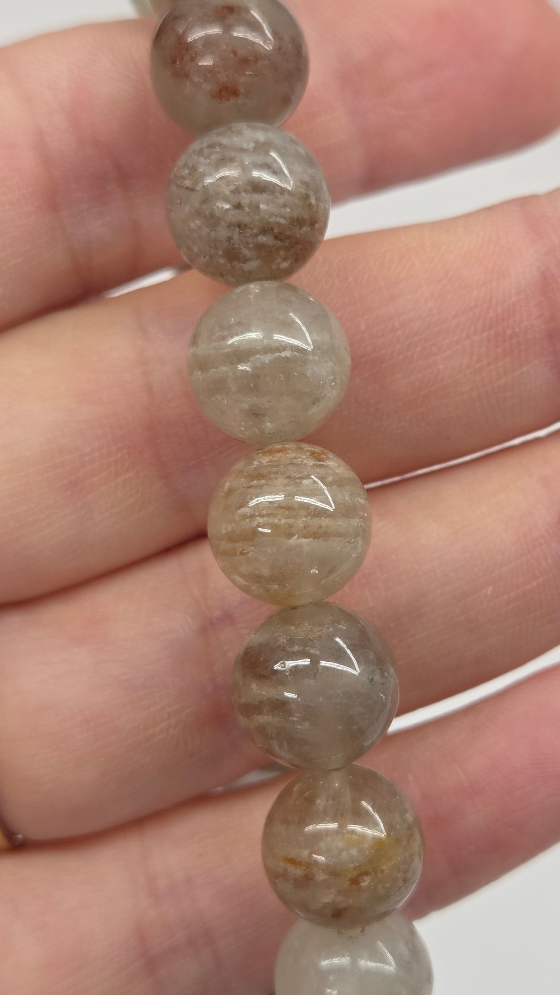 A close-up of a hand holding a strand of polished round beads made of translucent gray and brown stone, with a gold ring on one finger.