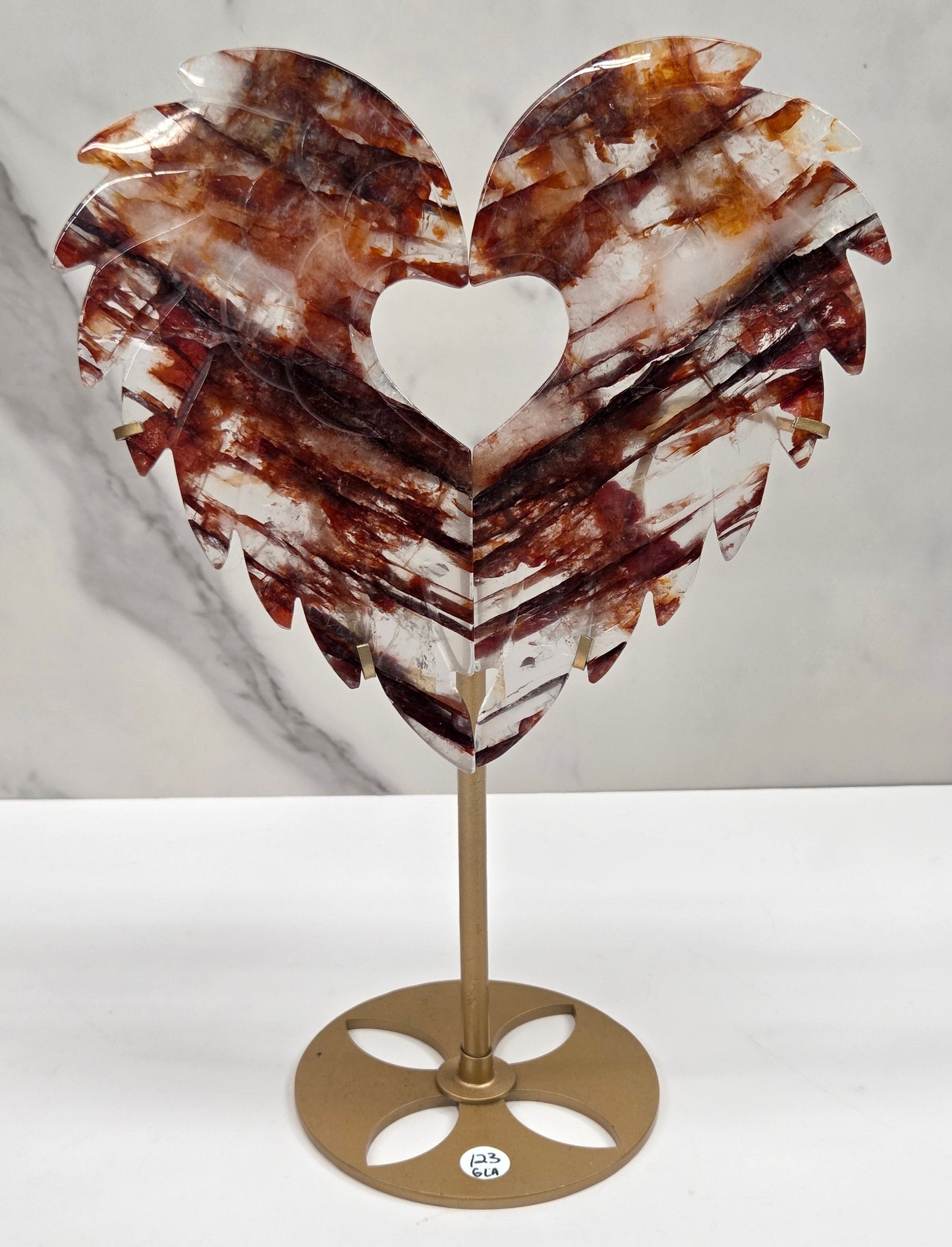 Decorative fire quartz heart-shaped  wing carvings on a gold stand against a white wall.