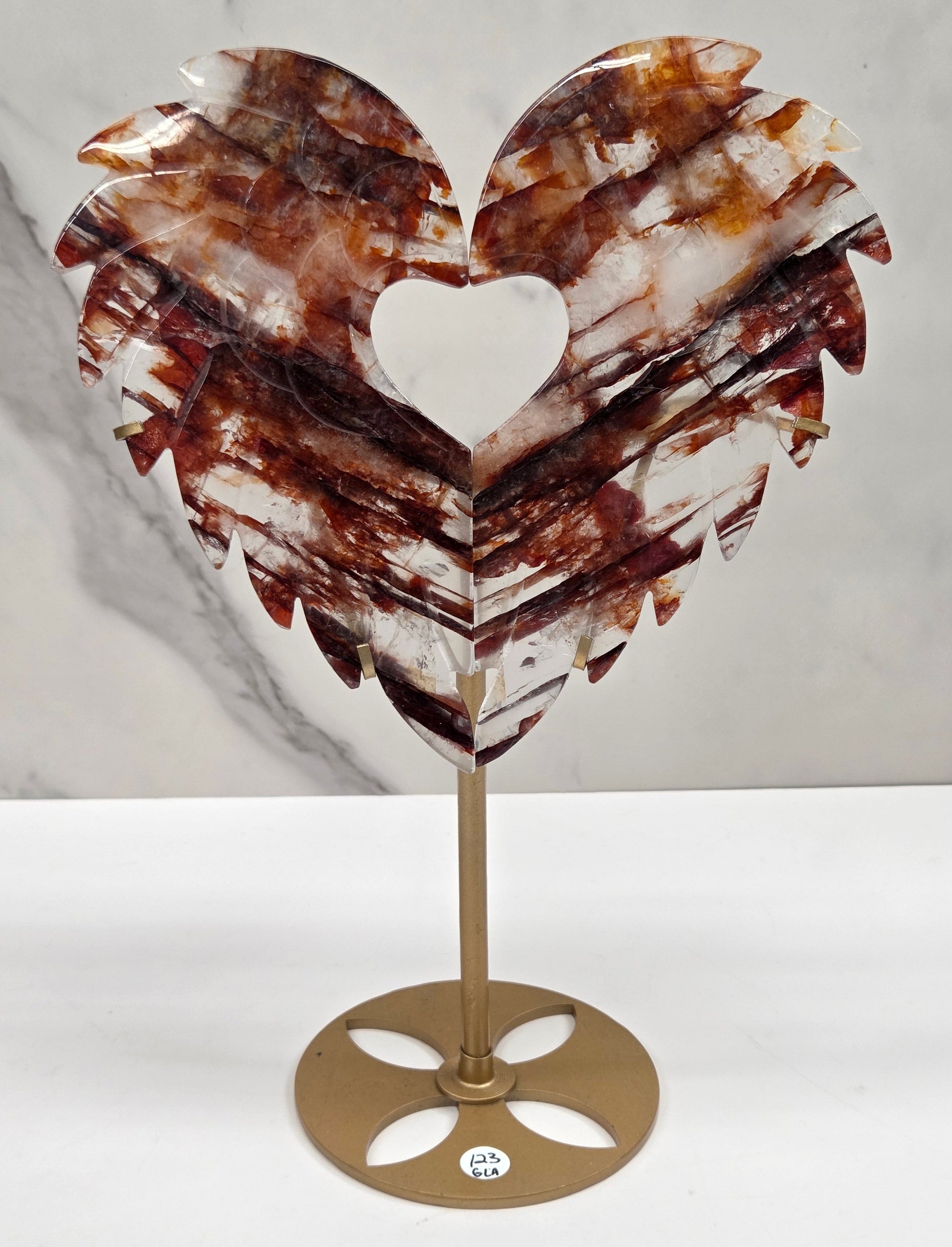 Decorative fire quartz heart-shaped  wing carvings on a gold stand against a white wall.