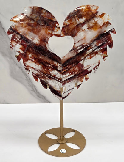 Decorative fire quartz heart-shaped  wing carvings on a gold stand against a white wall.