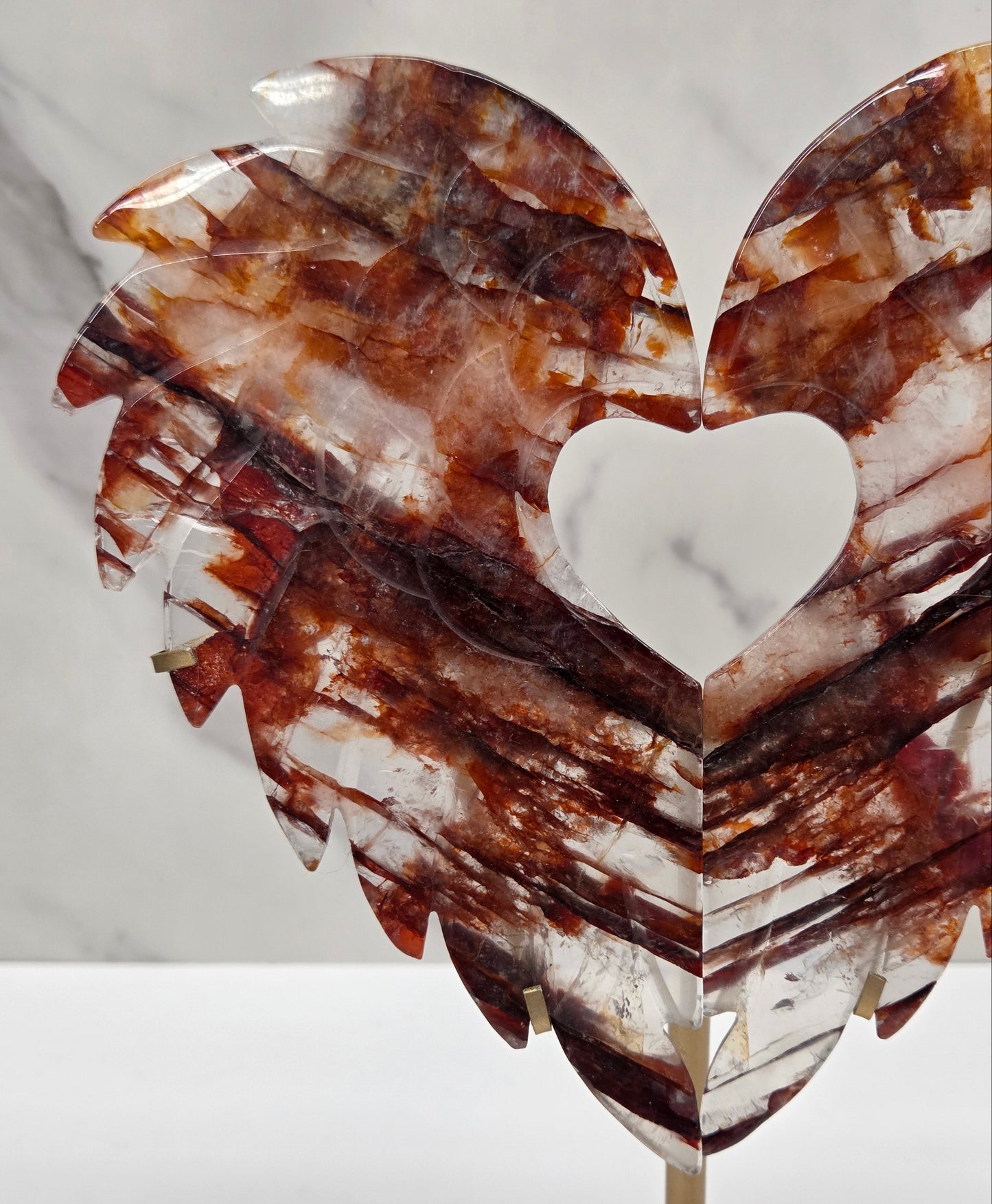 Decorative fire quartz heart-shaped  wing carvings on a gold stand against a white wall.