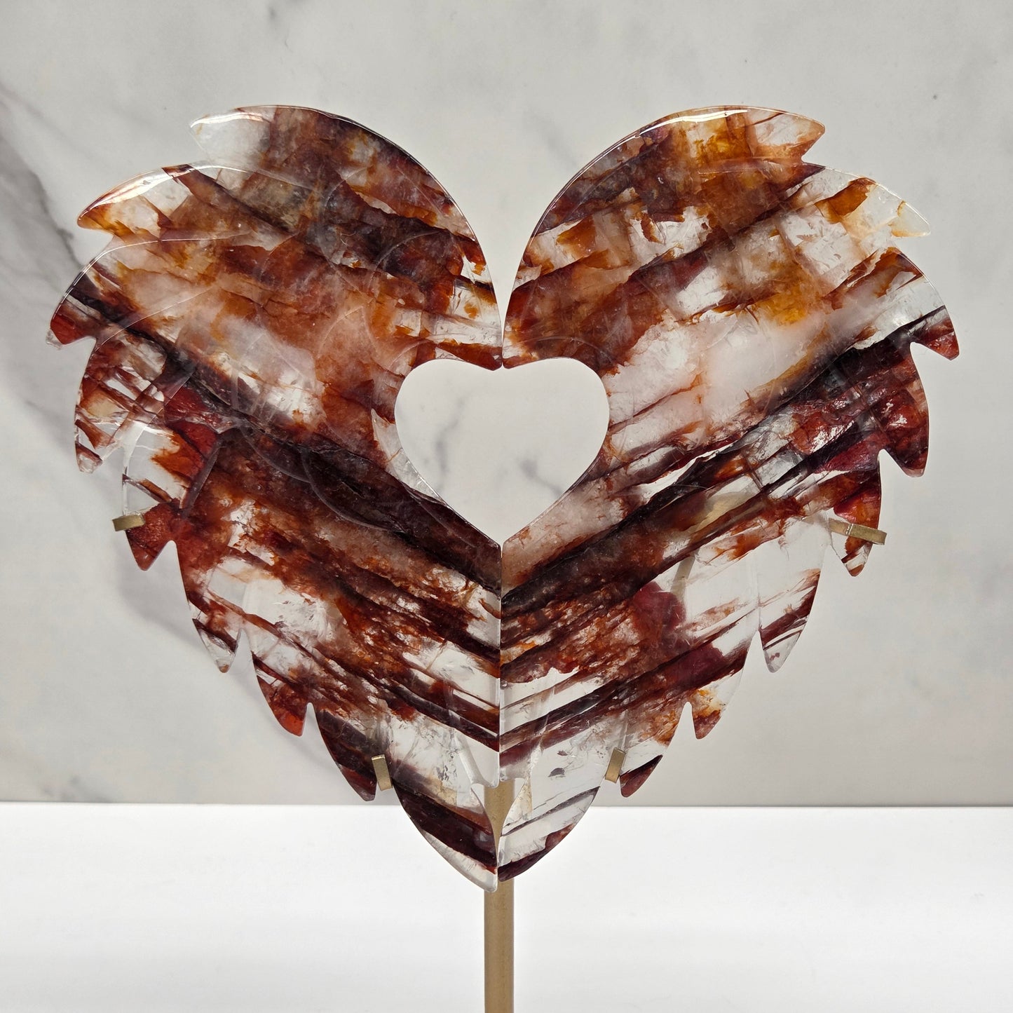 Decorative fire quartz heart-shaped  wing carvings on a gold stand against a white wall.