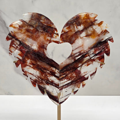 Decorative fire quartz heart-shaped  wing carvings on a gold stand against a white wall.