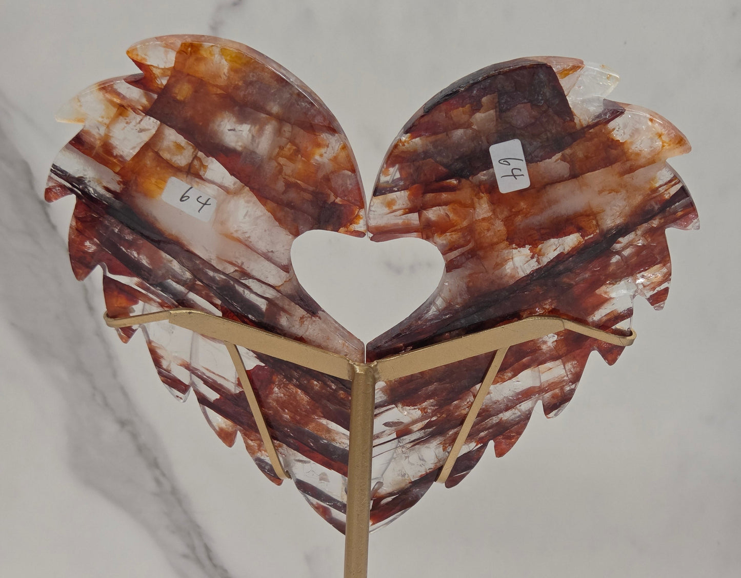 Decorative fire quartz heart-shaped  wing carvings on a gold stand against a white wall.