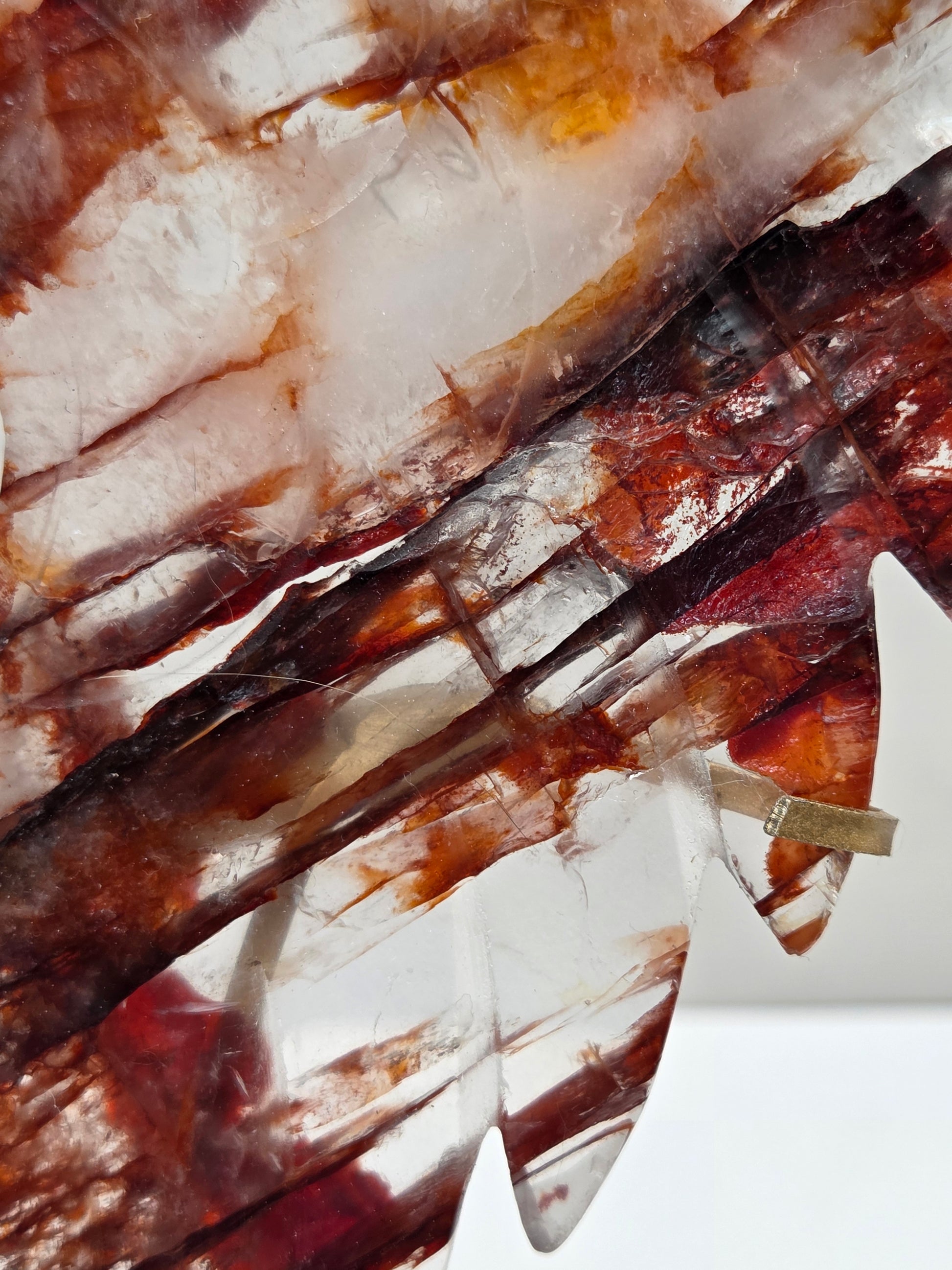 A close-up of a translucent decorative object with layered organic shapes in white, amber, and reddish-brown tones, with a small metallic clip visible near the top.
