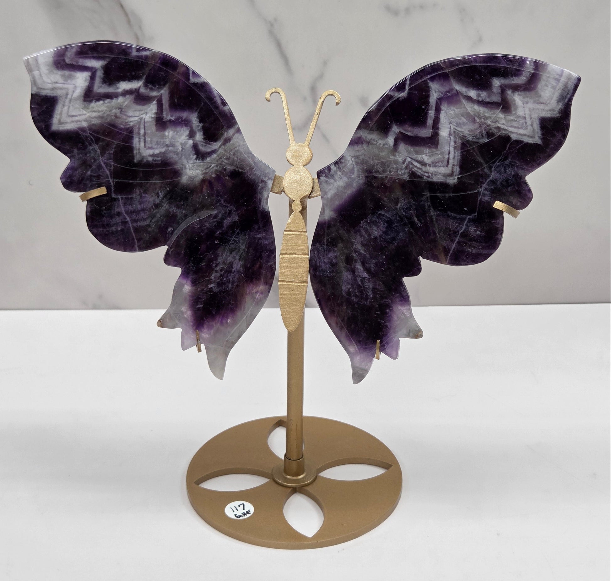 A decorative butterfly wall carving with dark purple and gray patterned wings mounted on a gold-toned metal bracket against a white wall.