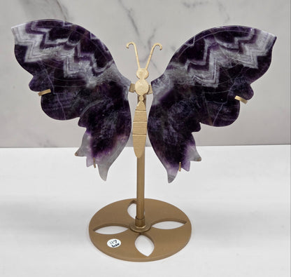 A decorative butterfly wall carving with dark purple and gray patterned wings mounted on a gold-toned metal bracket against a white wall.