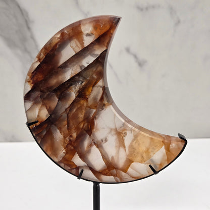 A crescent-shaped wall sconce with a polished brown and cream agate stone inlay, mounted on a black metal rod against a white marble wall.