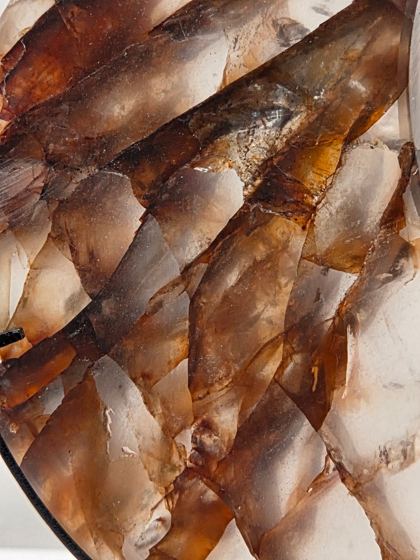 A close-up of a translucent stone or glass surface with layered irregular shapes in smoky brown, amber, cream, and gray tones.