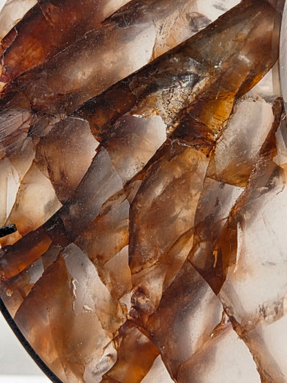 A close-up of a translucent stone or glass surface with layered irregular shapes in smoky brown, amber, cream, and gray tones.