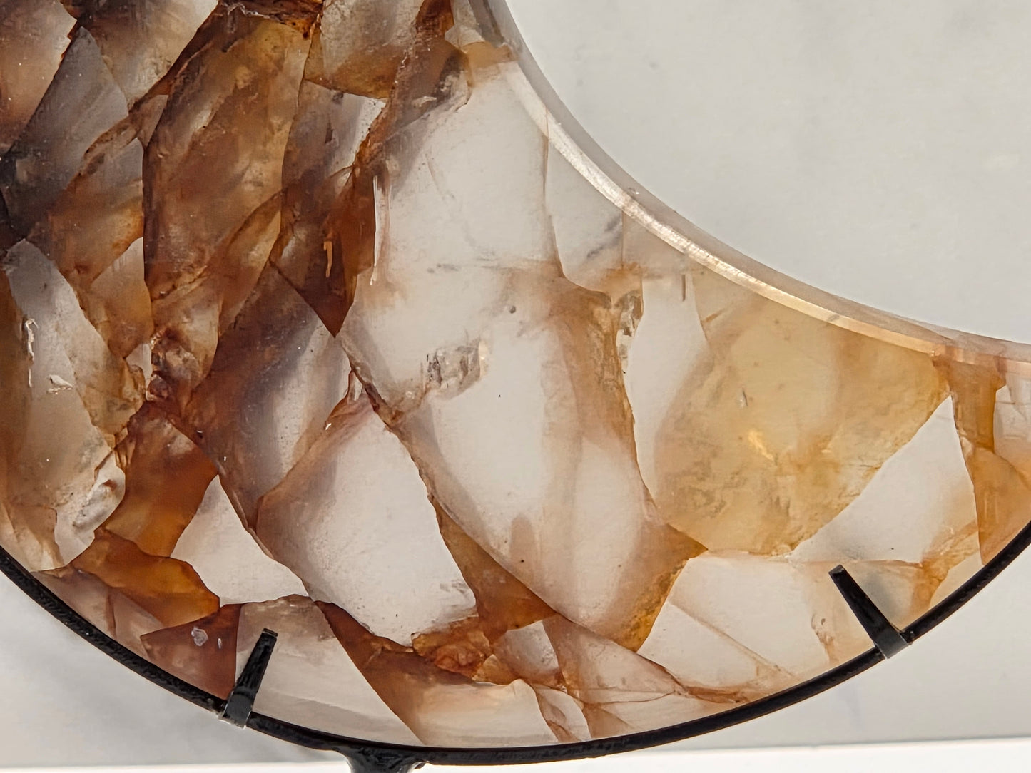 Close-up of a crescent-shaped decorative object featuring a natural agate or onyx stone inlay with layered translucent brown, tan, and cream crystalline patterns, mounted on a black circular base.