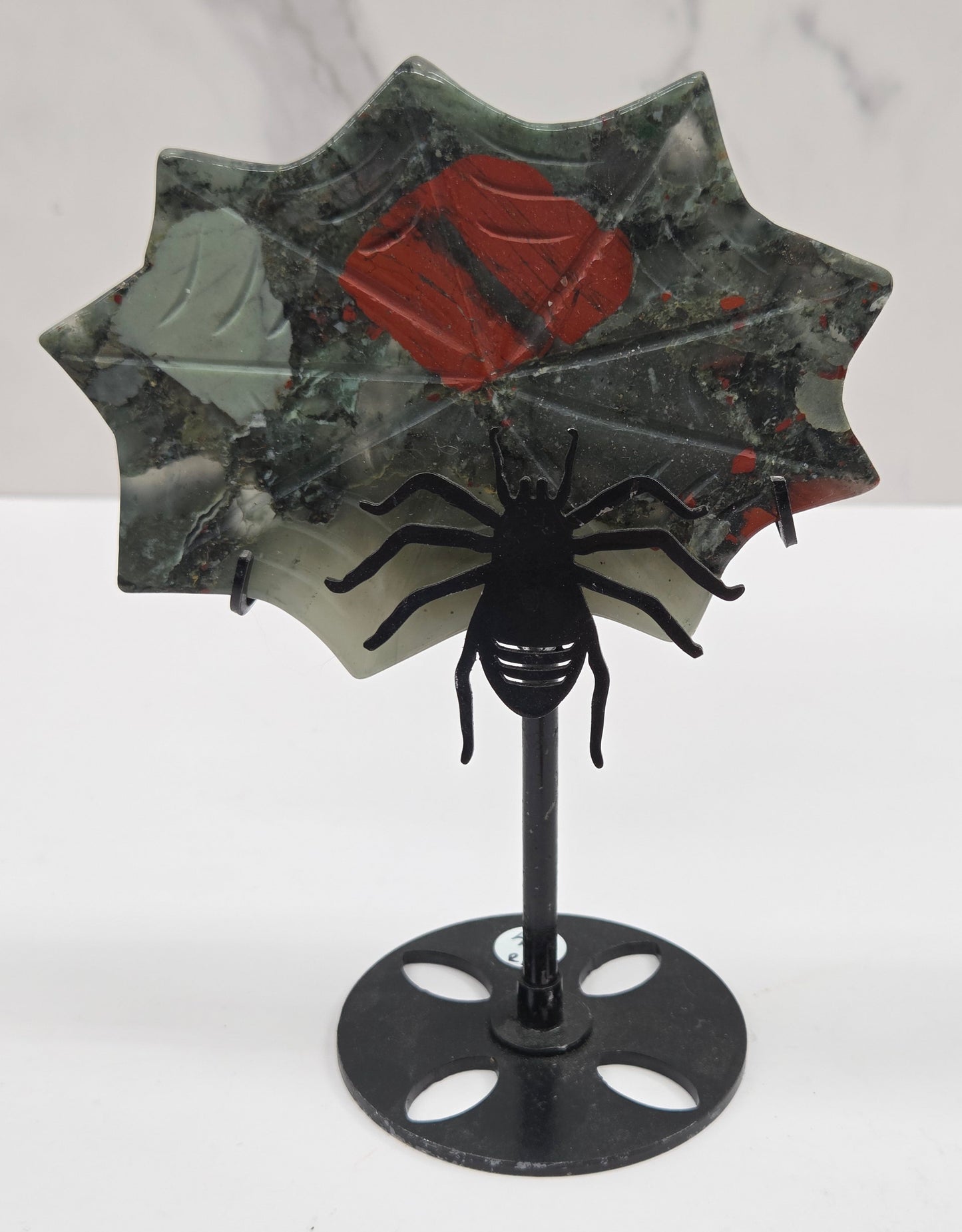A decorative spider web wall hanging with a black metal spider and web frame, mounted on a white wall next to a white marble-patterned surface.