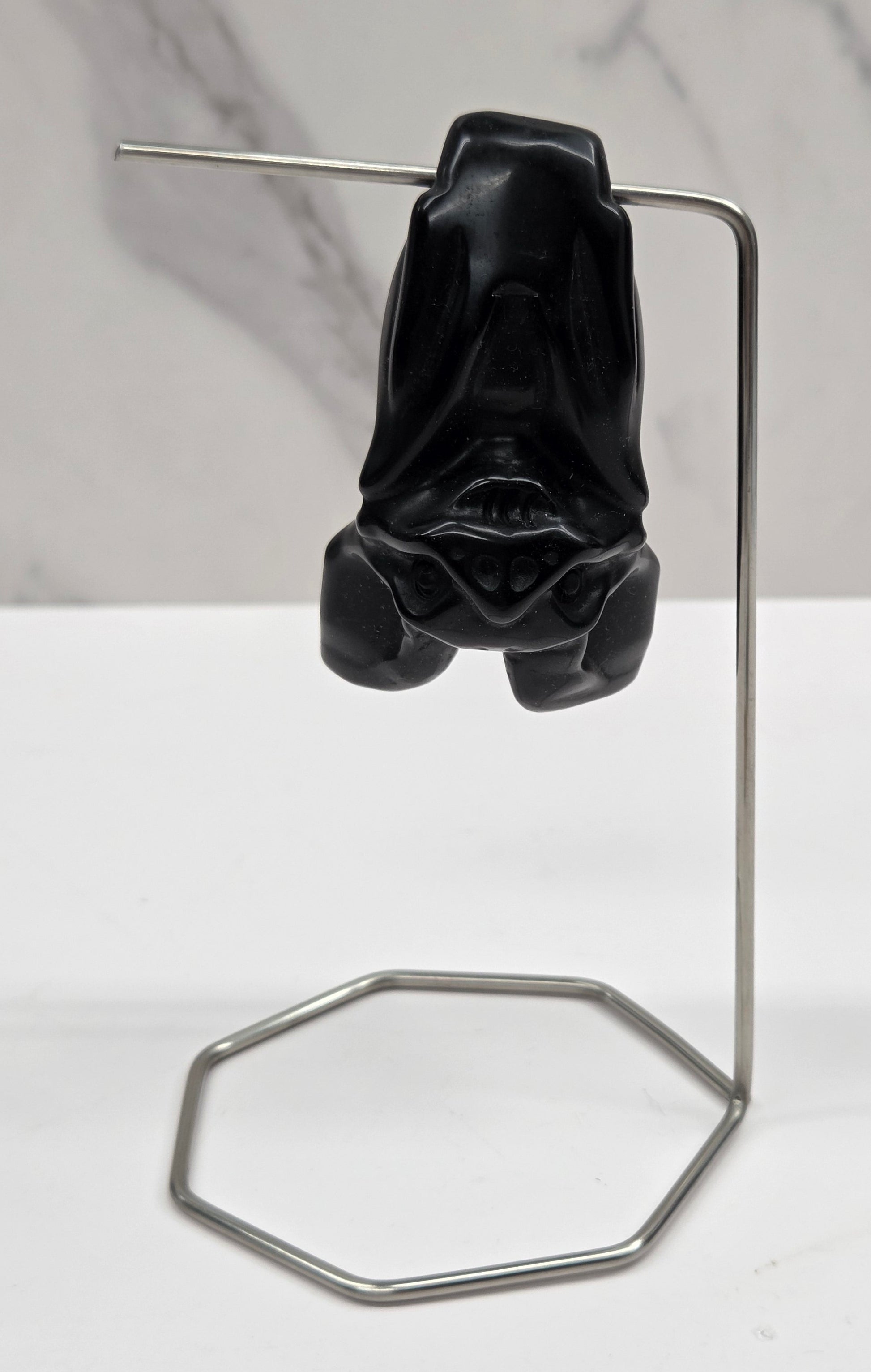 A black sculptural bat carving a long, thin metal frame and a hexagonal loop, photographed against a white and light gray marble-textured background.
