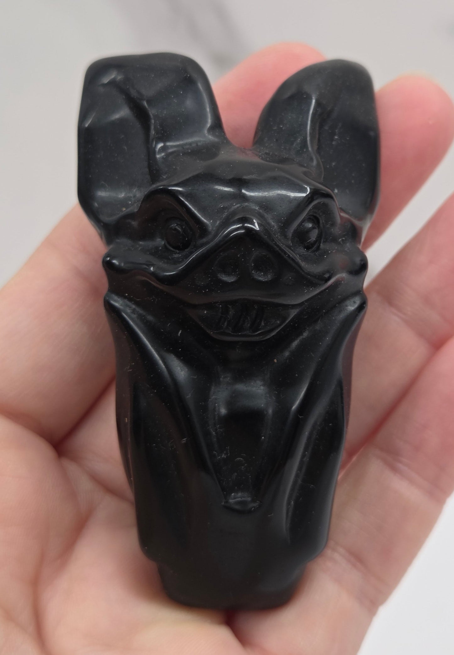 A hand holding a small black carved figurine with animal-like features, photographed against a light marble-patterned background.