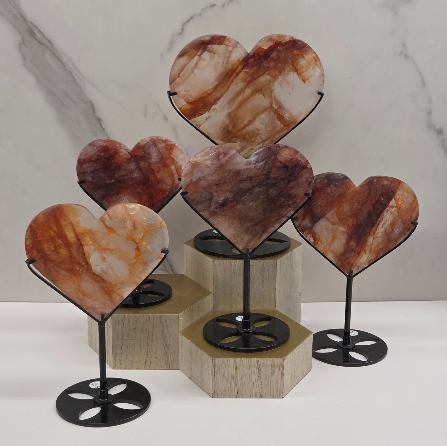 Collection of Fire Quartz hearts black stands, shown against a white wall and marble-patterned background.