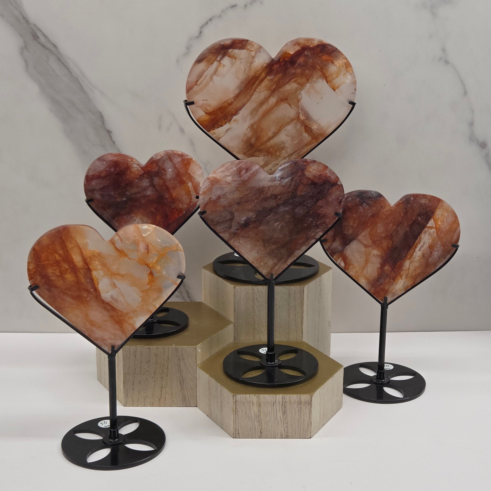 Collection of Fire Quartz hearts black stands, shown against a white wall and marble-patterned background.