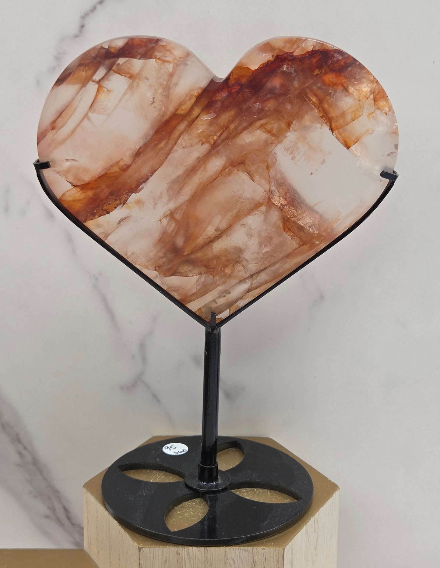 Fire Quartz heart on a black stand, shown against a white wall and marble-patterned background.
