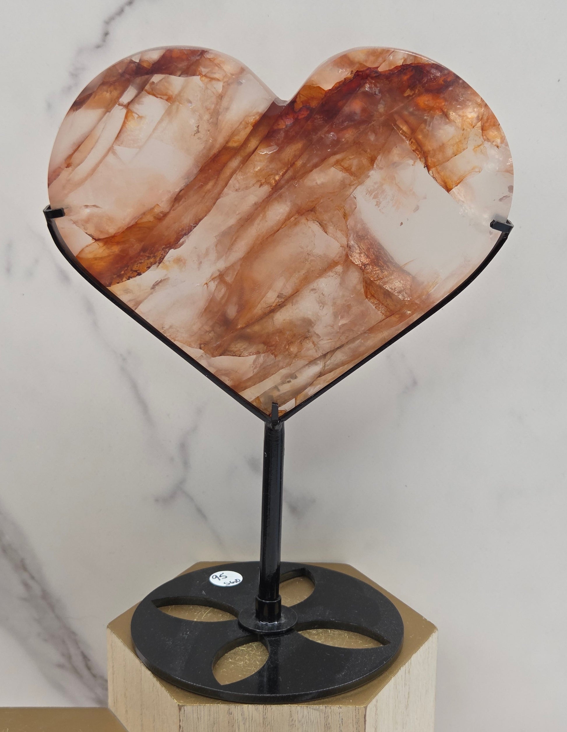Fire Quartz heart on a black stand, shown against a white wall and marble-patterned background.