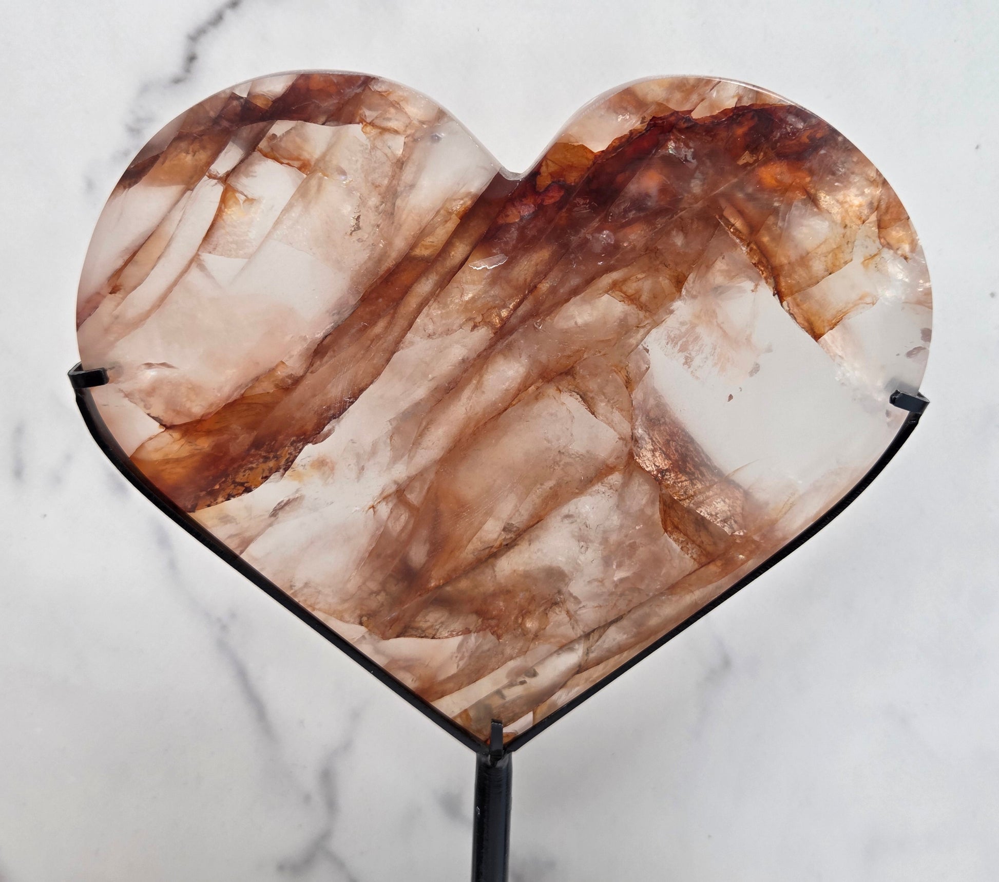 Fire Quartz heart on a black stand, shown against a white wall and marble-patterned background.