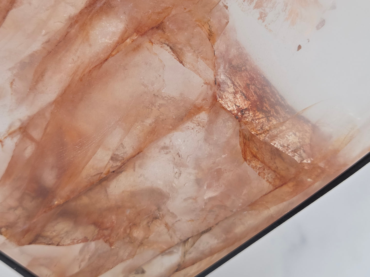 A close-up of a translucent pale pink stone or crystal with natural marbling and a metallic coppery highlight near the upper right edge.