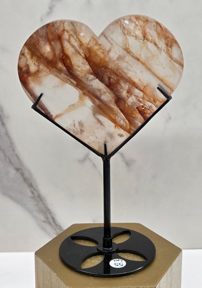 Fire Quartz heart on a black stand, shown against a white wall and marble-patterned background.