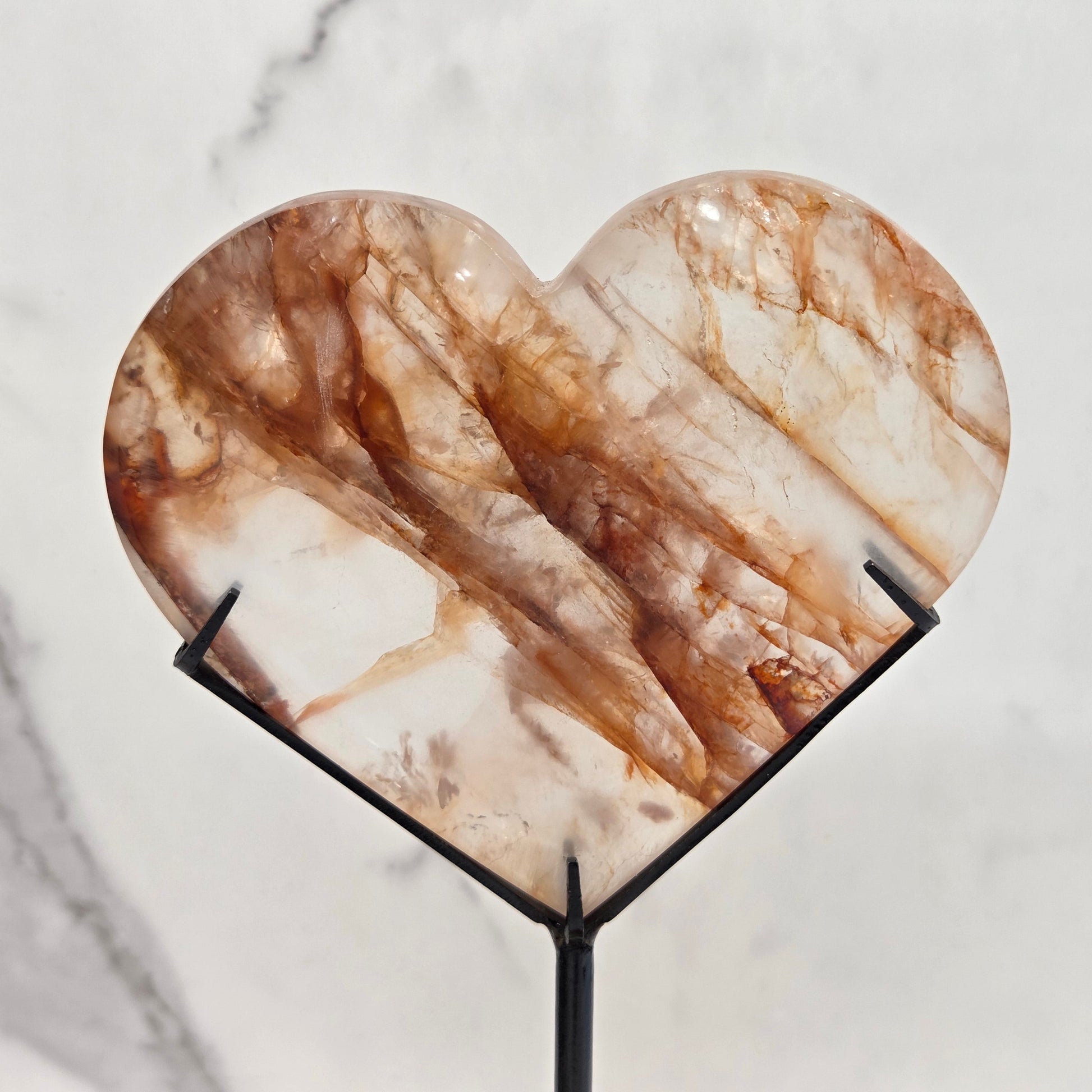 Fire Quartz heart on a black stand, shown against a white wall and marble-patterned background.