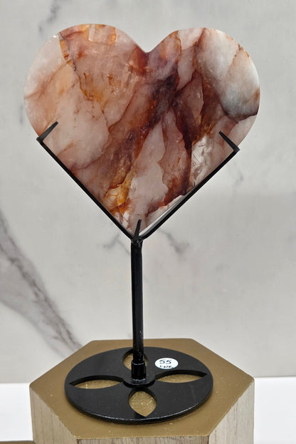 Fire Quartz heart on a black stand, shown against a white wall and marble-patterned background.