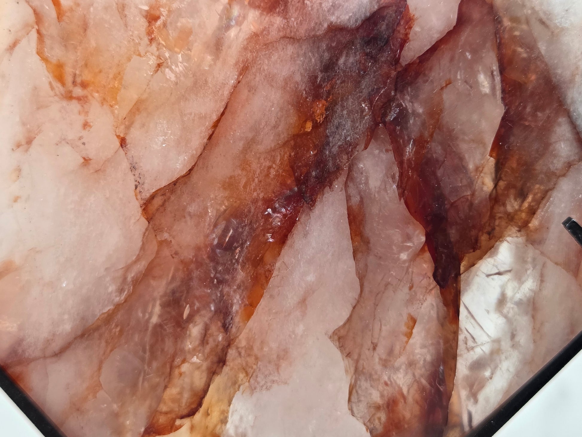 A close-up of a polished stone slab with layered translucent pink, peach, and dark brown crystalline patterns.