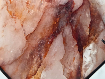 A close-up of a polished stone slab with layered translucent pink, peach, and dark brown crystalline patterns.