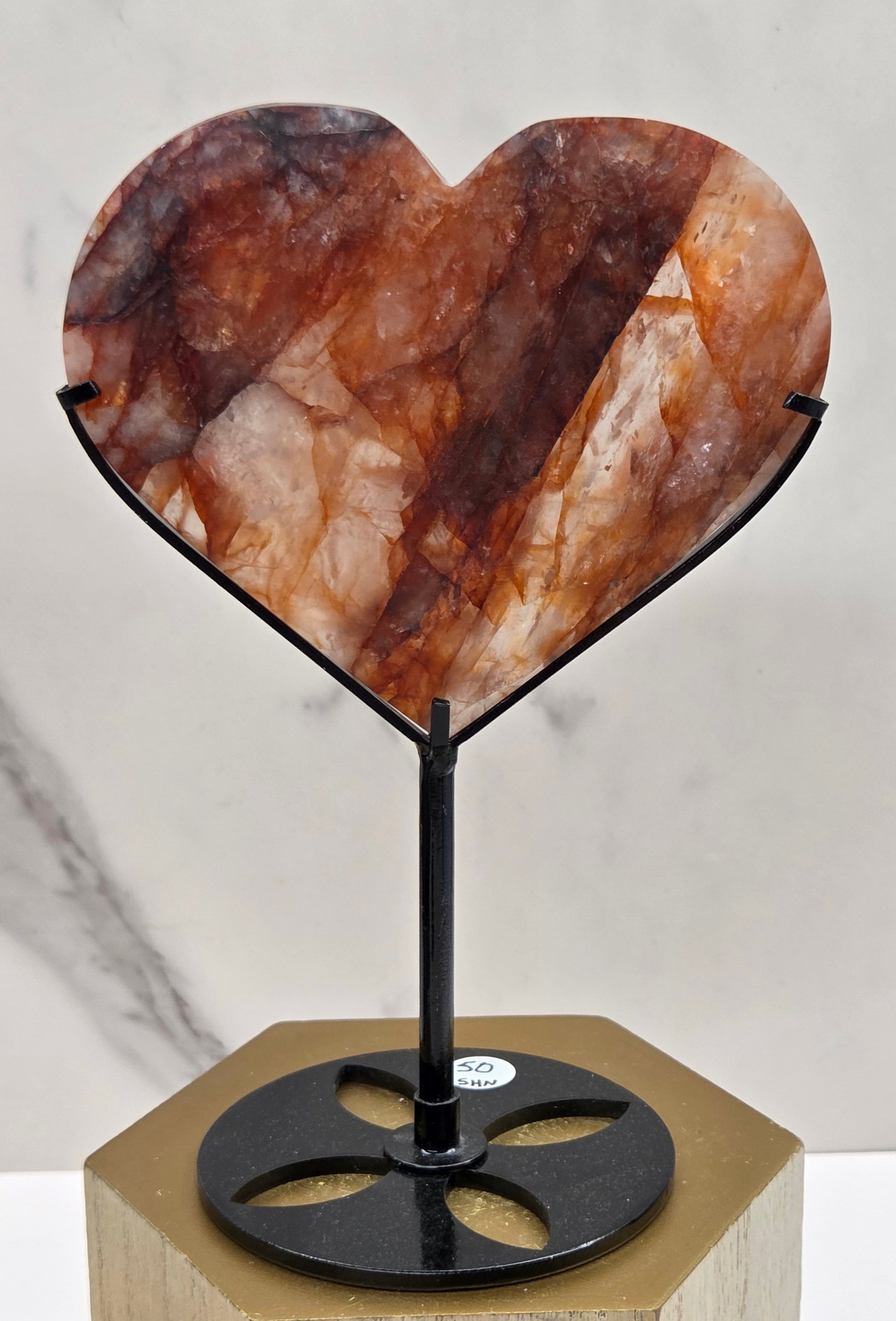 Fire Quartz heart on a black stand, shown against a white wall and marble-patterned background.